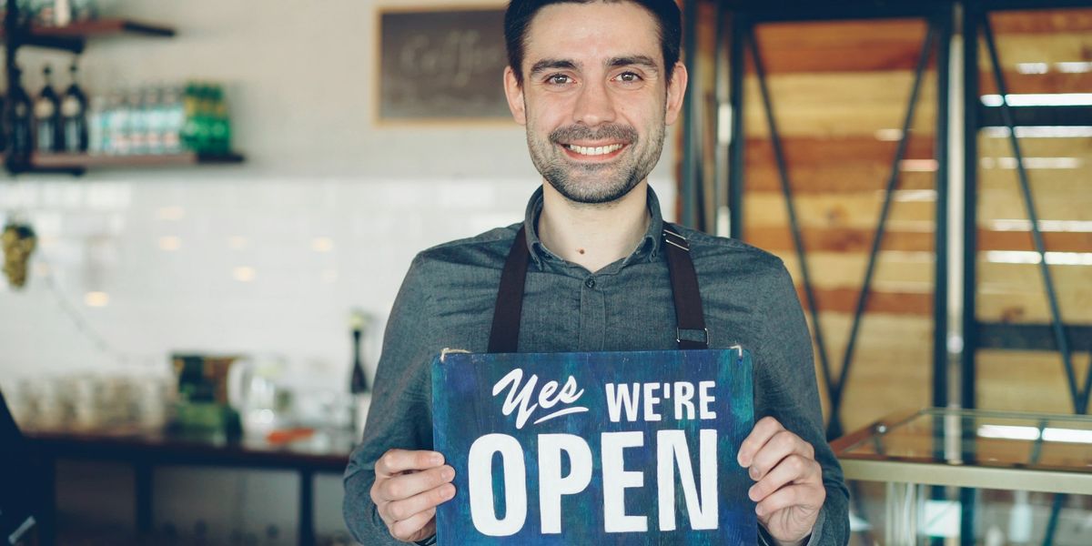 A barista holding an open sign in a cafe