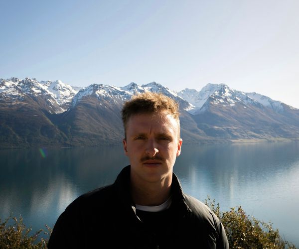 A man standing in front of a New Zealand lake and mountains