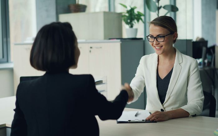 Two business owners shaking hands across a desk