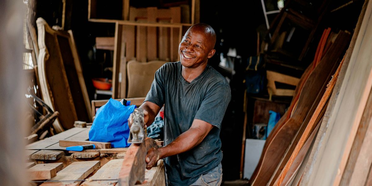 A joiner smiling as he works on a piece of timber in his workshop